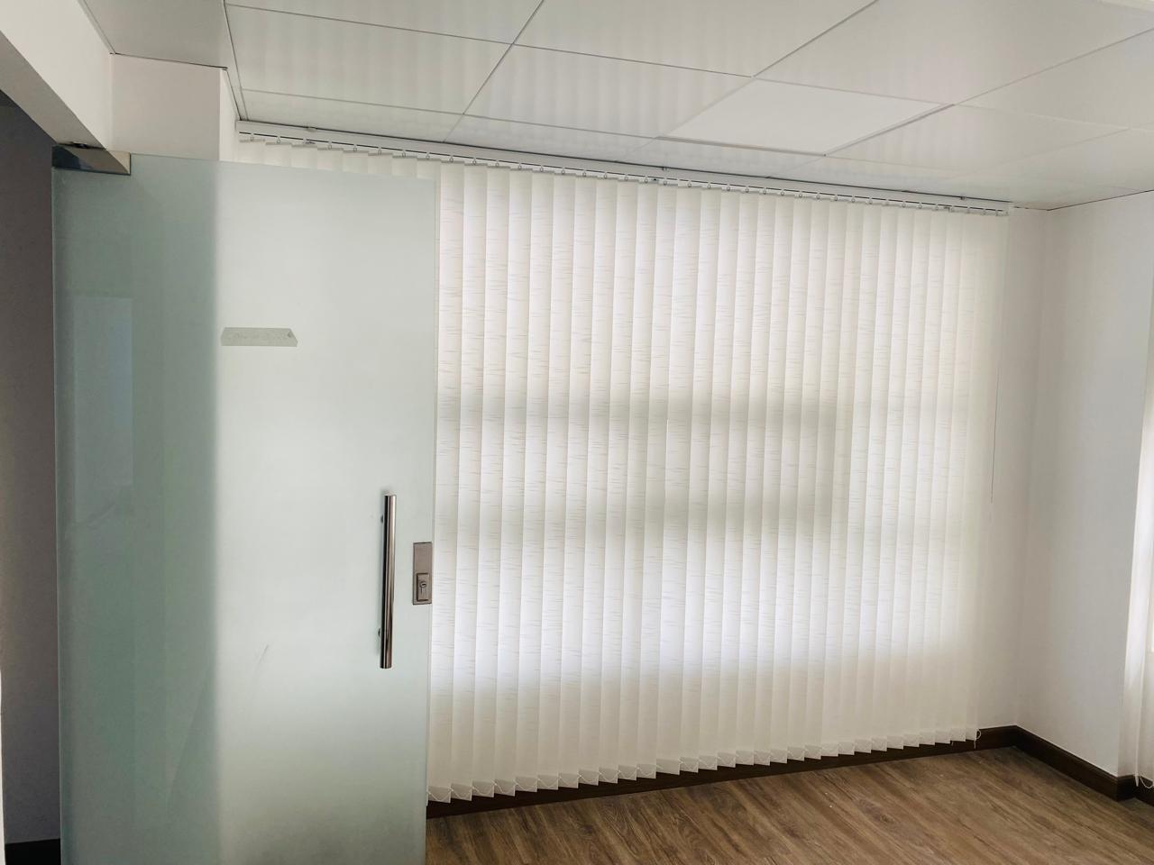 Glass-partitioned office bay fitted with vertical blinds