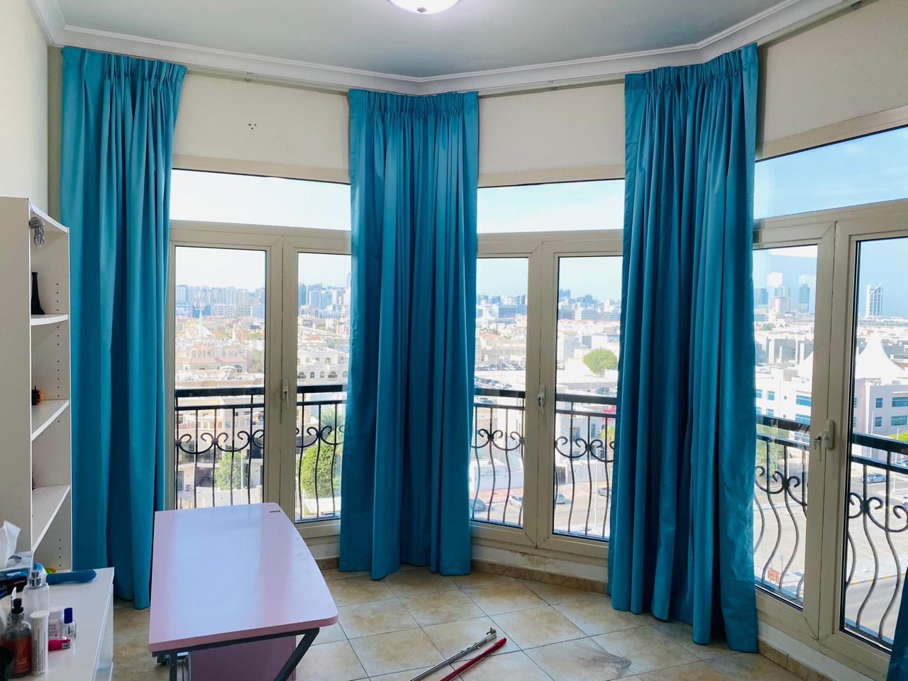 Floor-to-ceiling teal curtains framing a bay window over the Abu Dhabi skyline